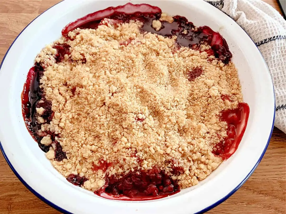 Round white pie dish with baked summer berry crumble.