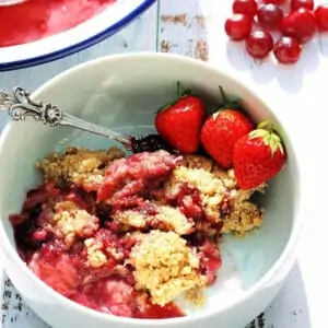 Close up of a bowl of berry crumble with strawberries in a white bowl.