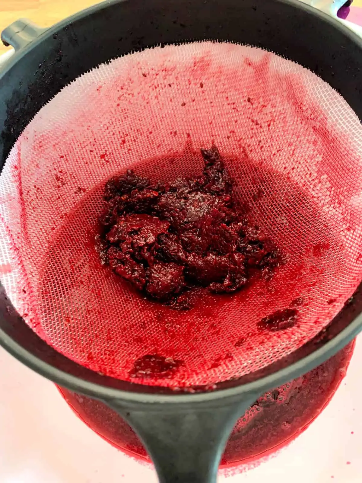Remains of blackcurrant puree in a sieve, only dry material remaining.