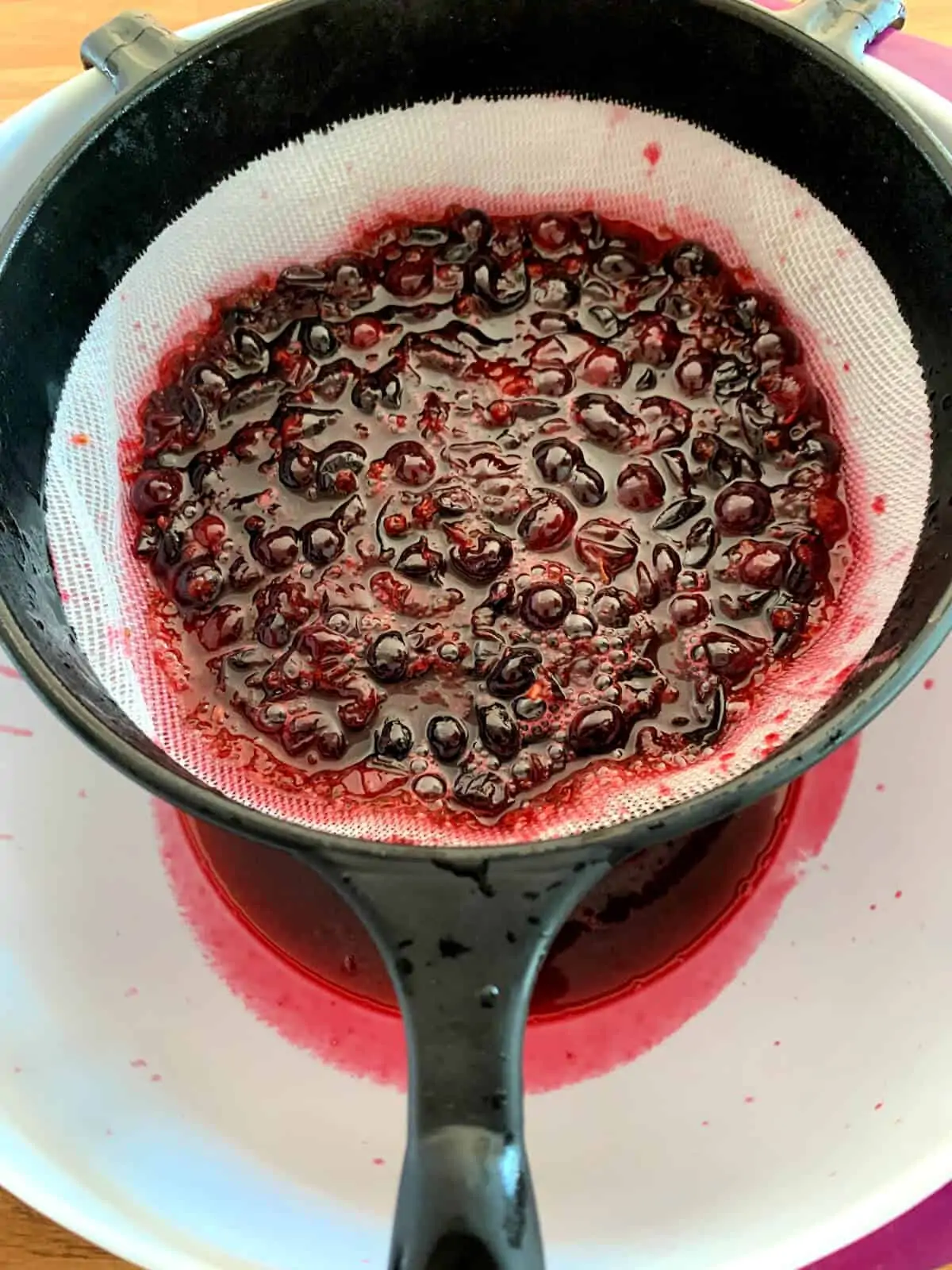 Sieving blackcurrants in syrup into a bowl.