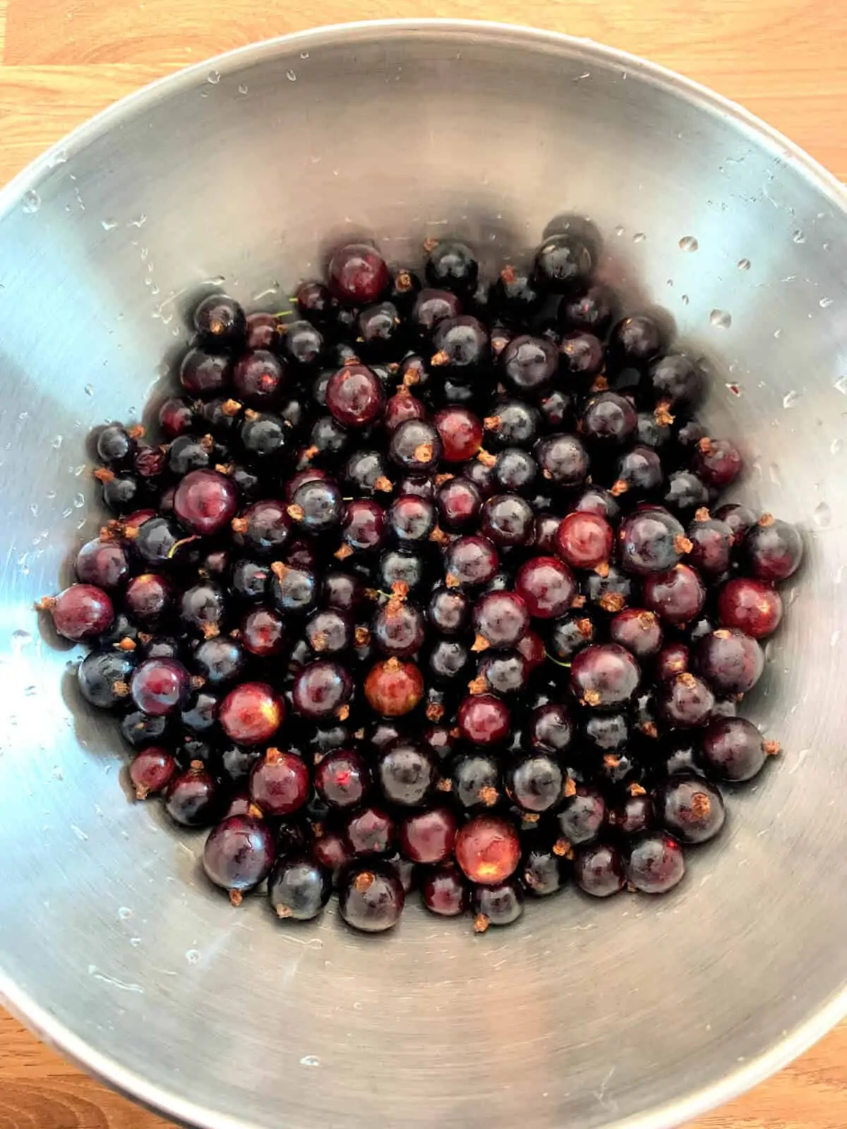 Washed blackcurrants in a metal bowl.