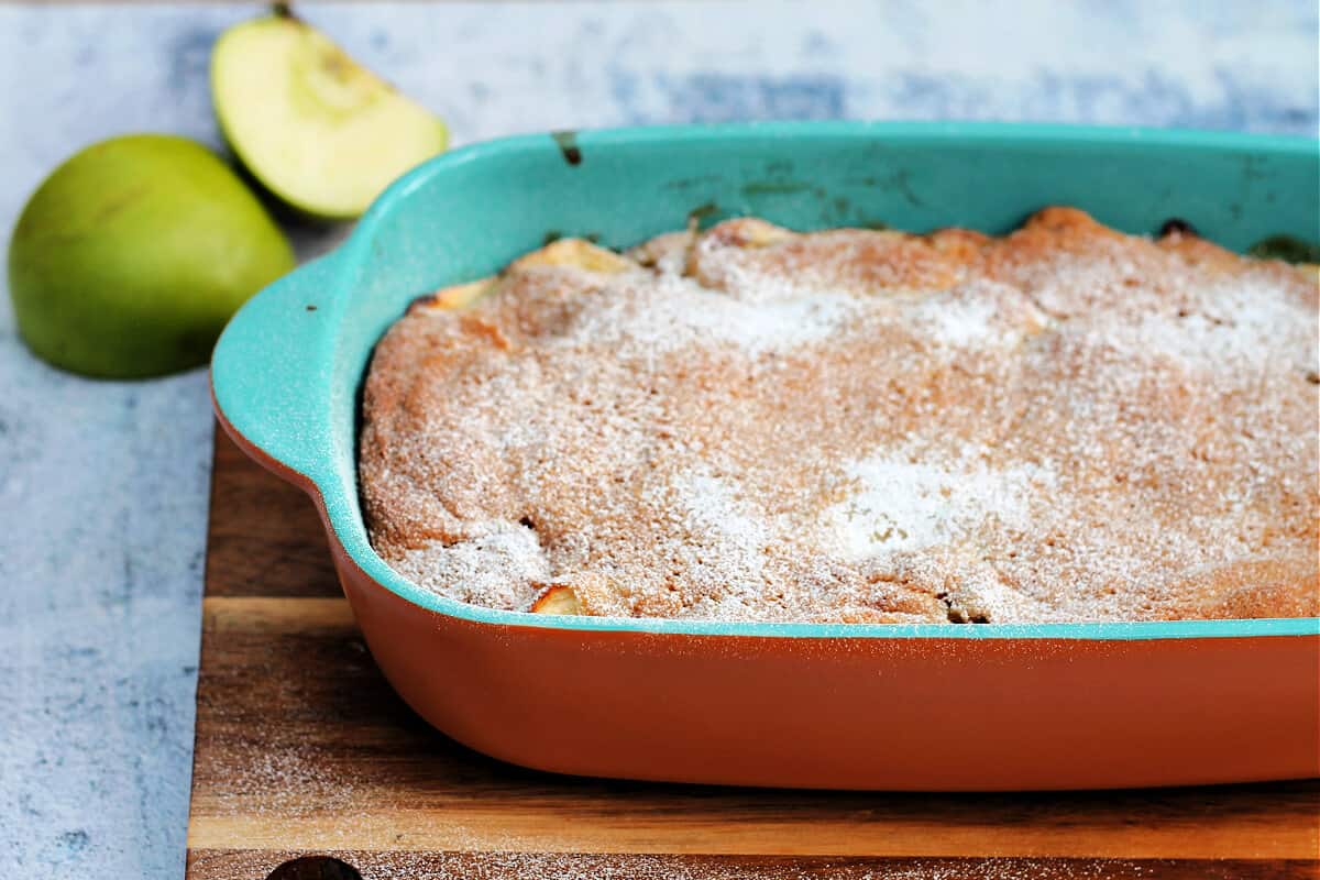 Light blue serving dish with apple sponge pudding topped with a dusting of icing sugar.