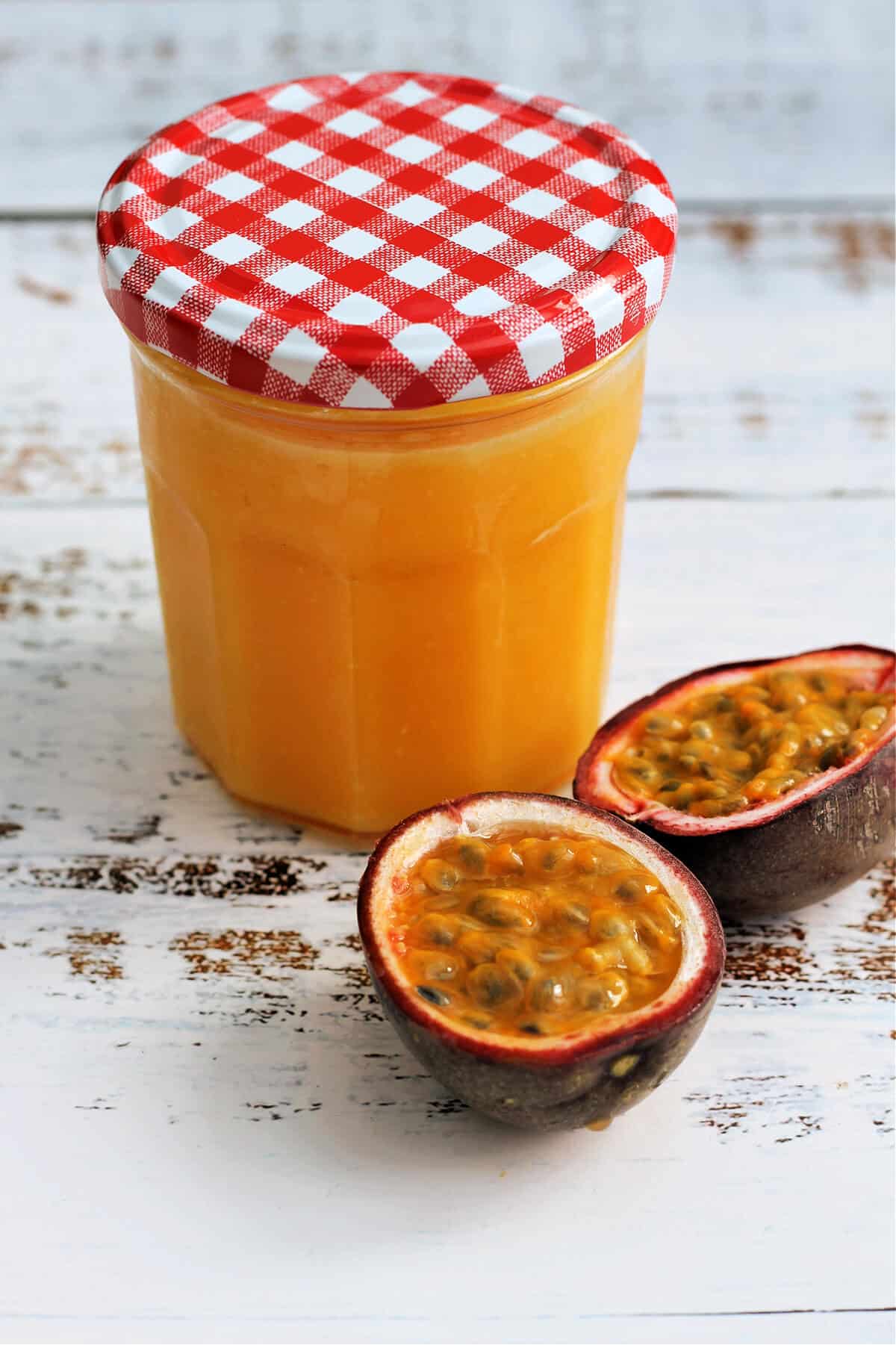 Jar of orange coloured curd on a table with some passionfruit.