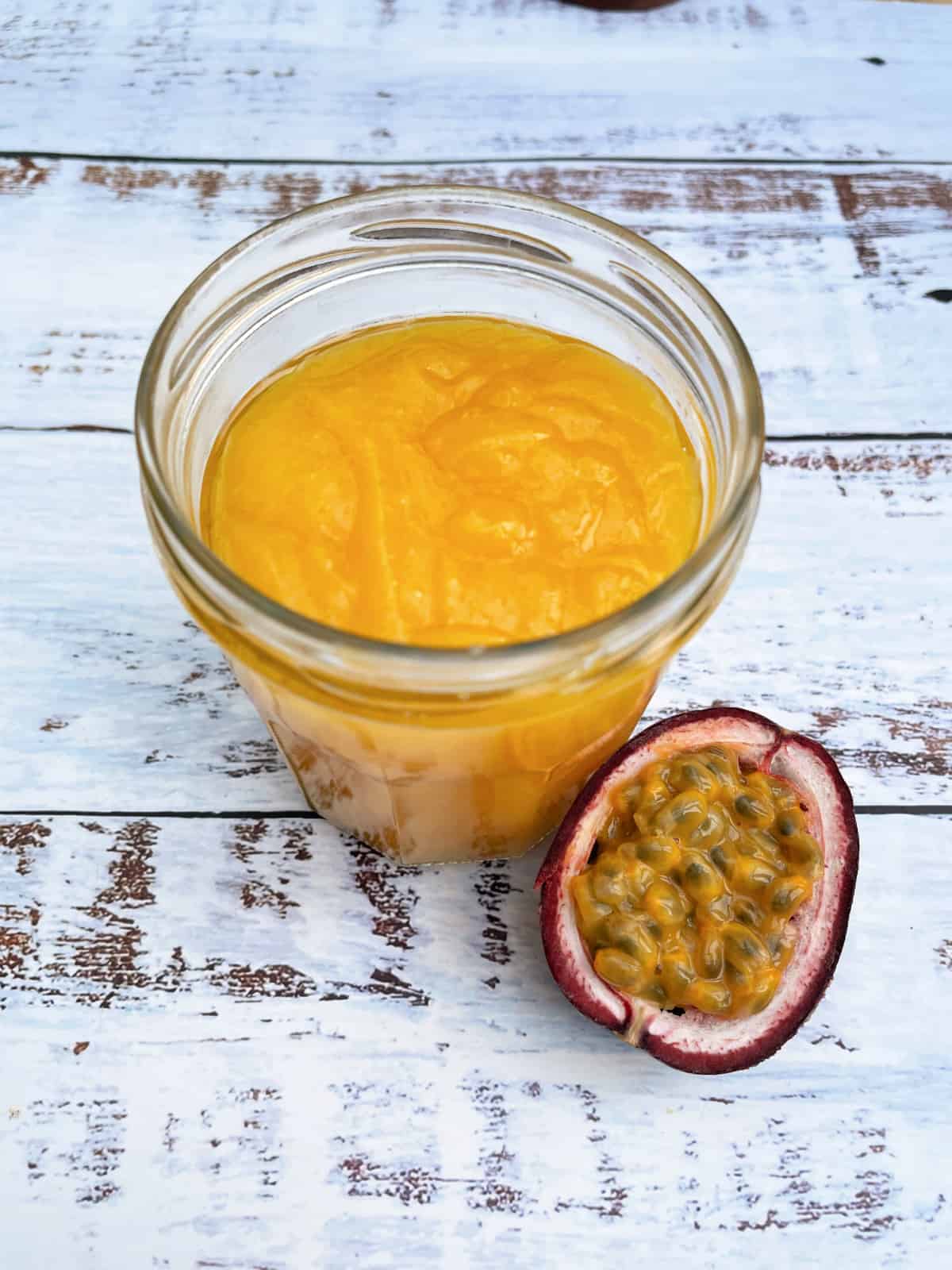 Jar of passionfruit curd with half a passionfruit on the side.
