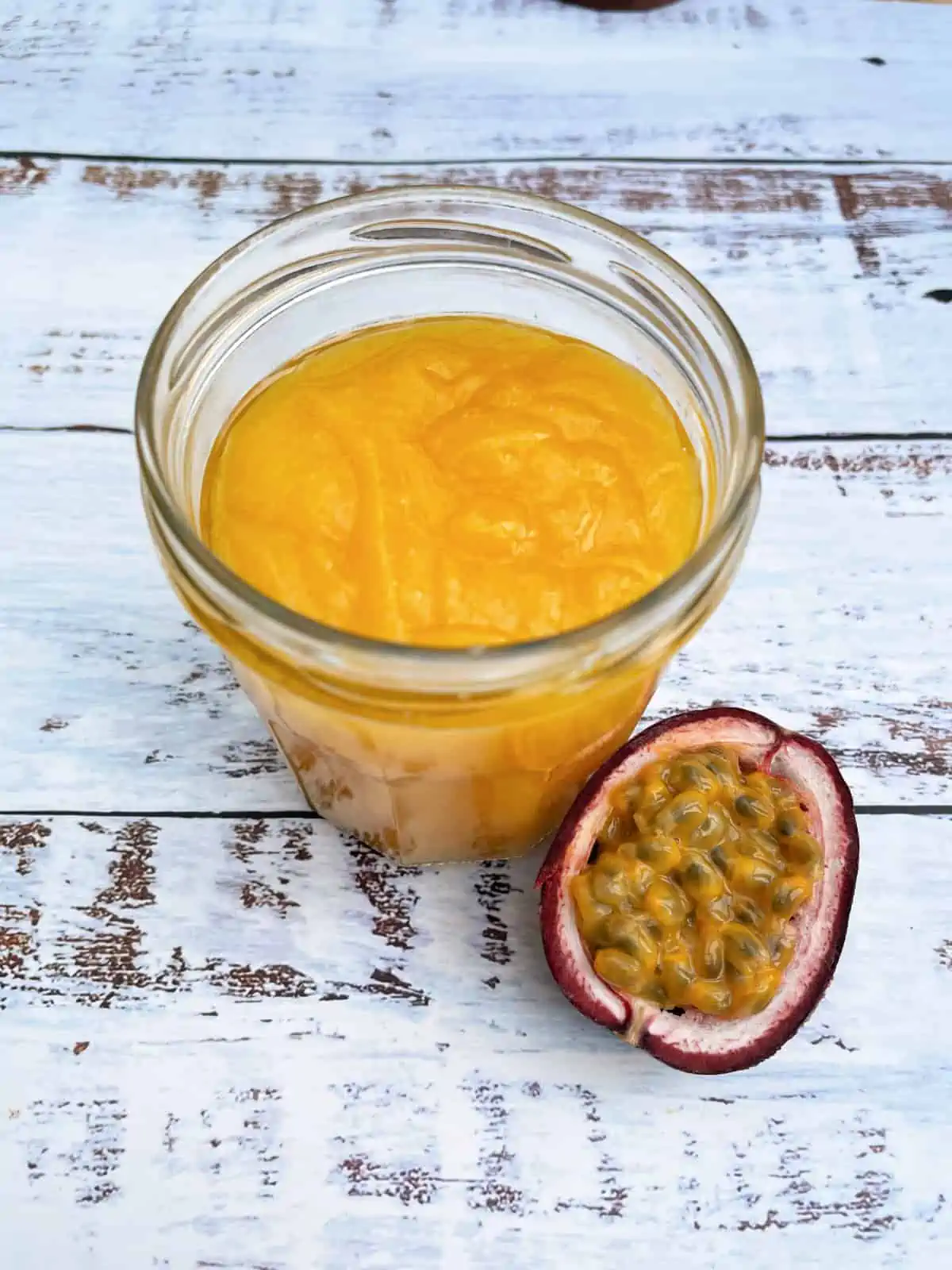 Jar of passionfruit curd with half a passionfruit on the side.