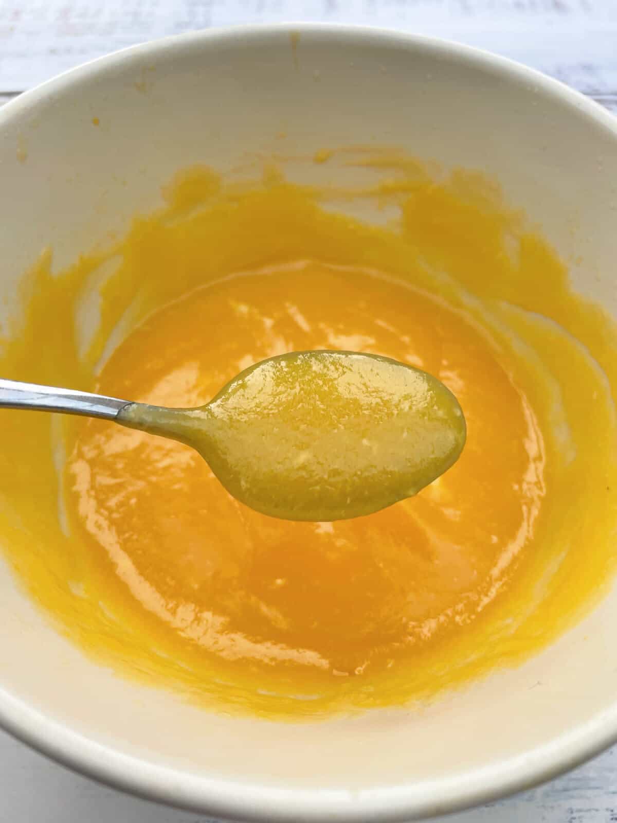 Passionfruit curd in  a bowl with a spoon showing the curd coating the spoon.