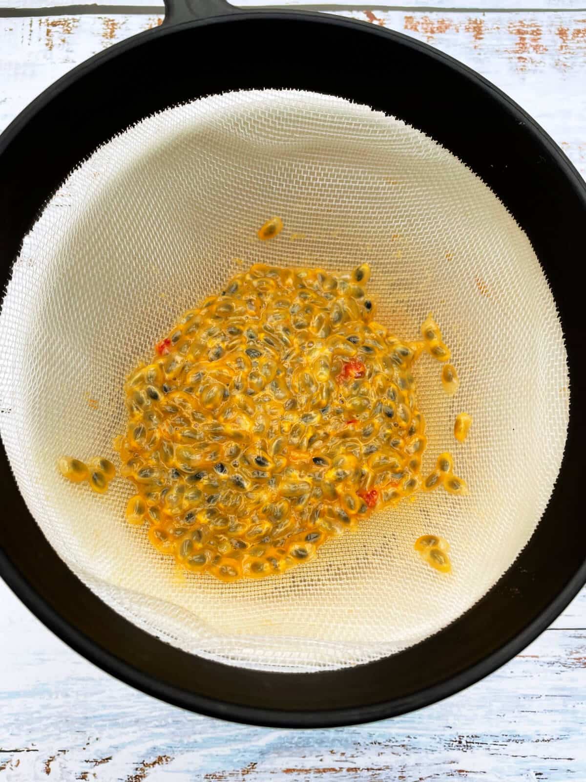 Sieve over a bowl containing passionfruit pulp.