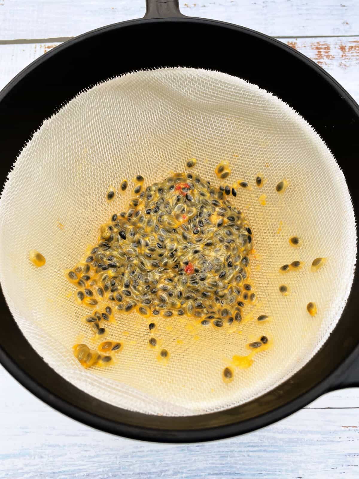 Sieve over a bowl containing passionfruit seeds.