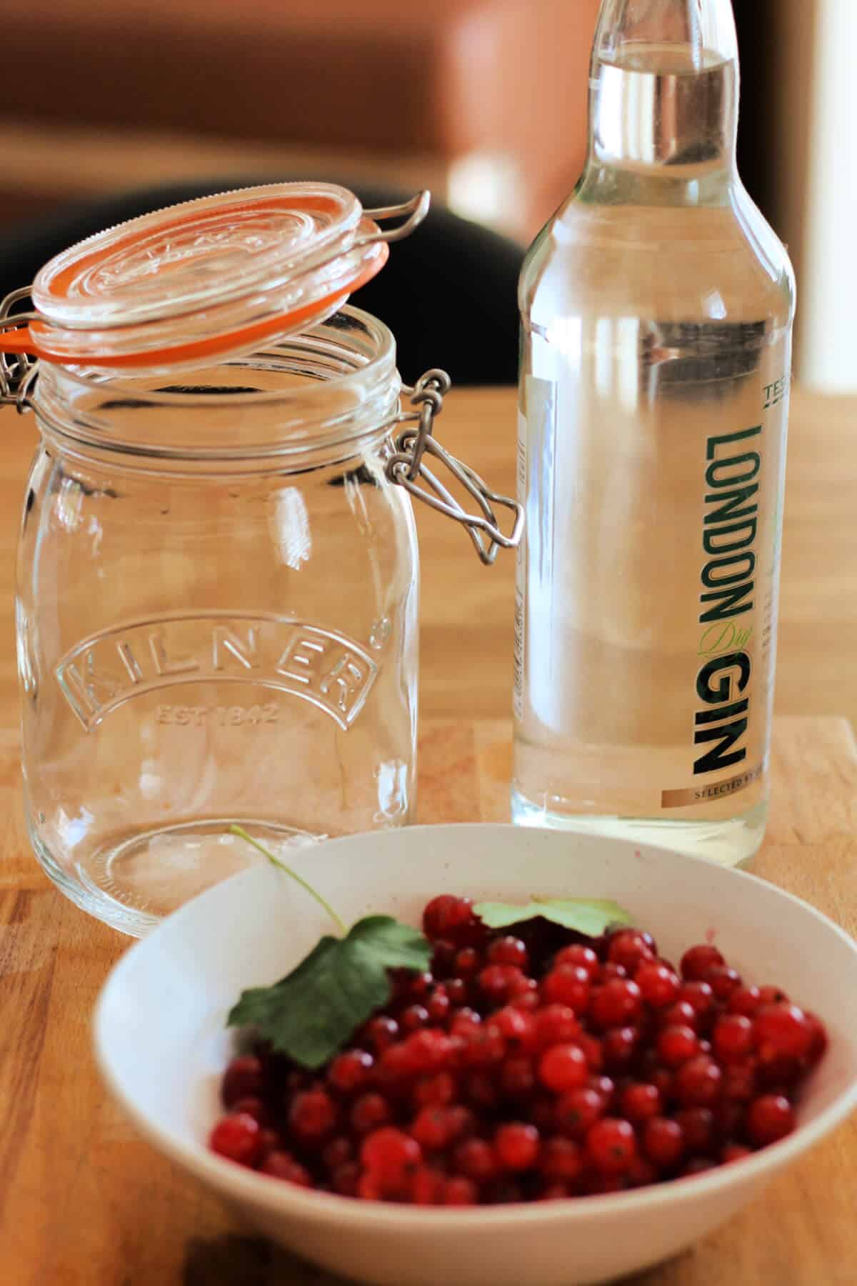 A bottle of gin, a mason jar and a bowl of redcurrants.