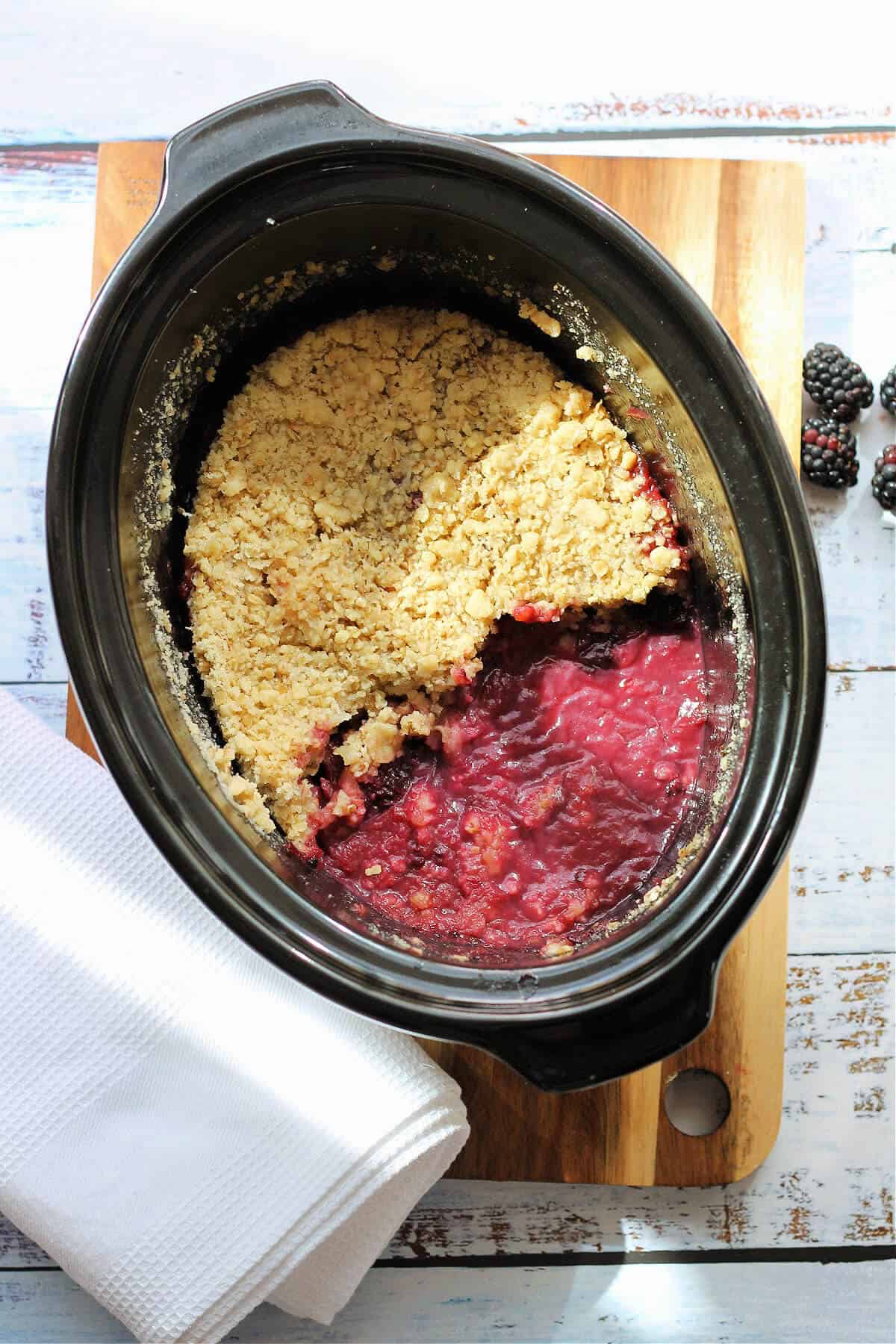 Deep red blackberry crumble in a black slow cooker pot.