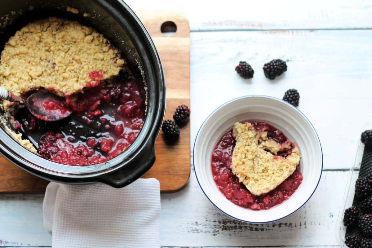 Slow cooker pot with crumble, with a bowl of crumble to the side.