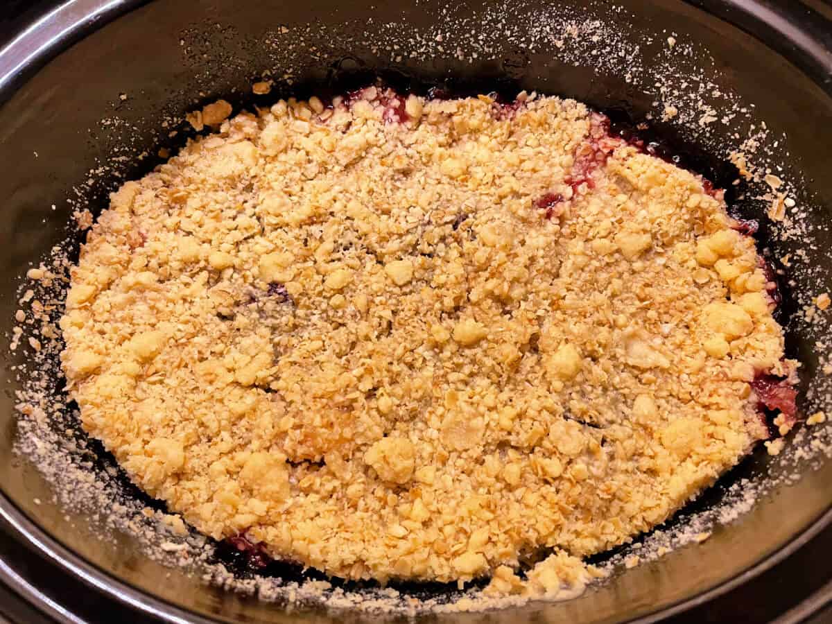 Cooked blackberry crumble in slow cooker pot.