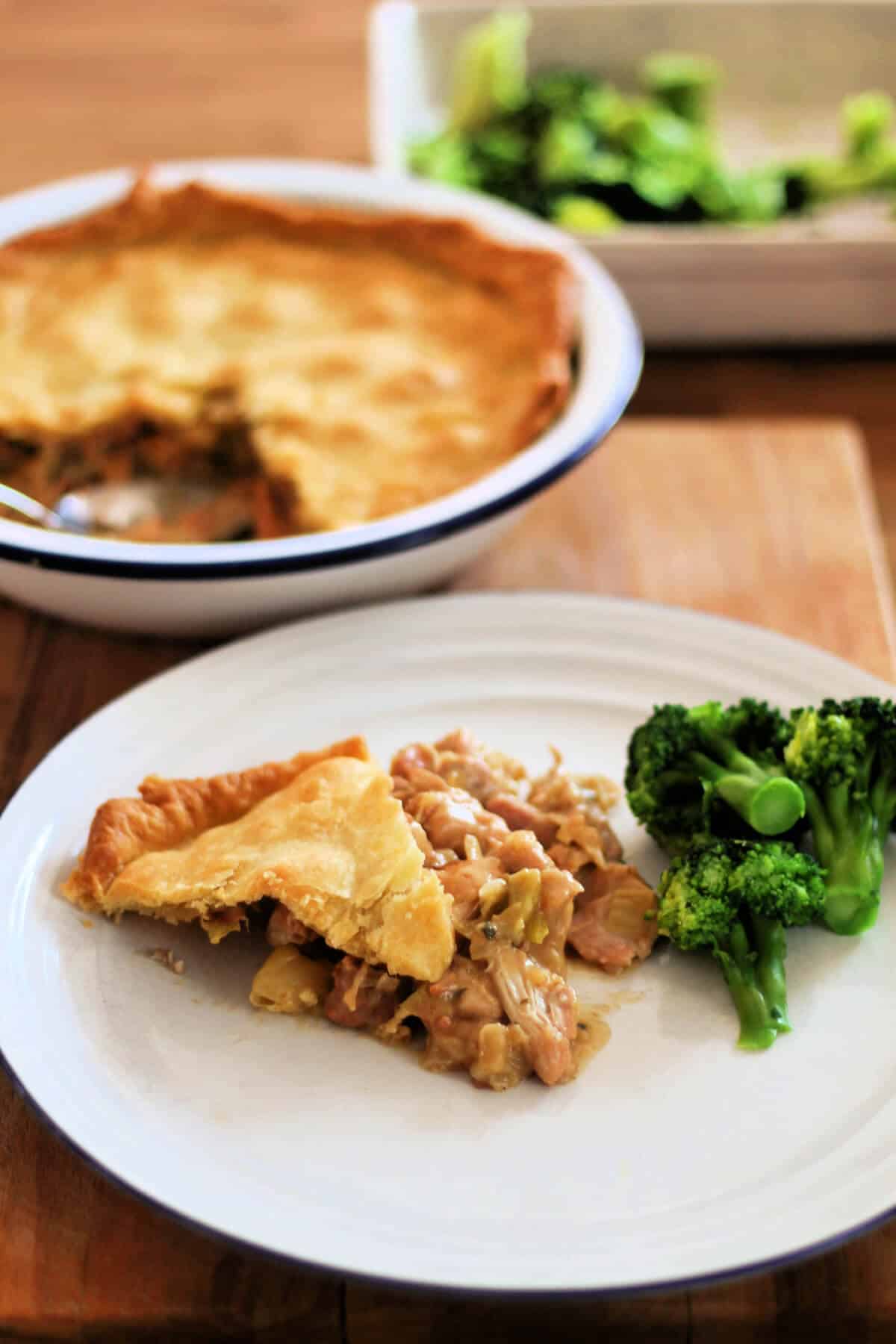 Chicken pie served on white plate, with broccoli, serving dish behind.