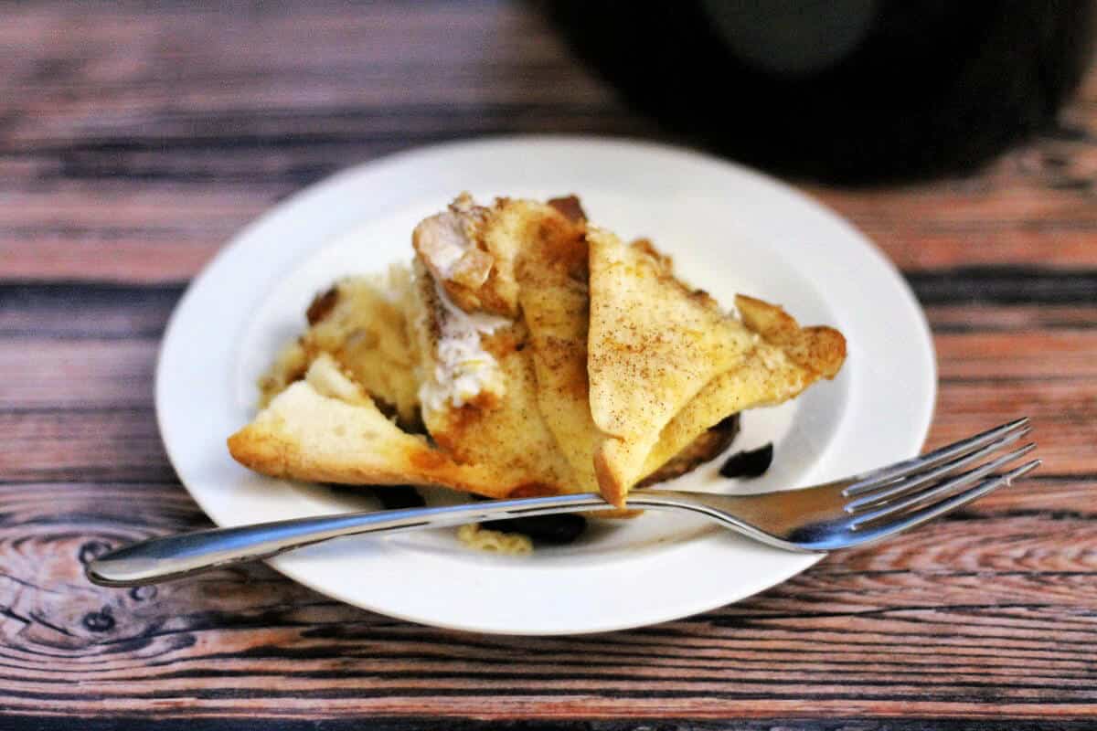 Serving of bread and butter pudding on a white plate with cream, with a fork.