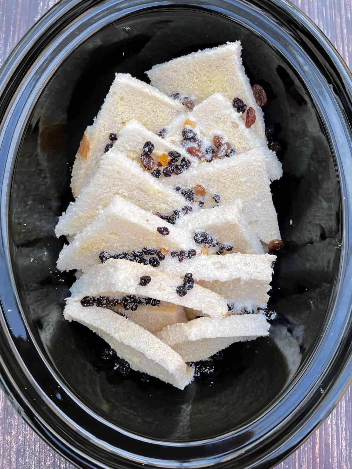Second layer of bread and dried fruit in slow cooker pot.