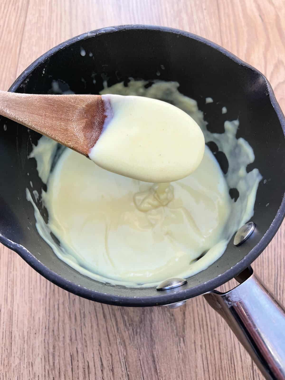 A thick cheese sauce in a saucepan, with a wooden spoon.