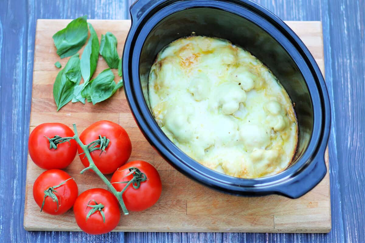 Cauliflower cheese casserole in dish with tomatoes beside.