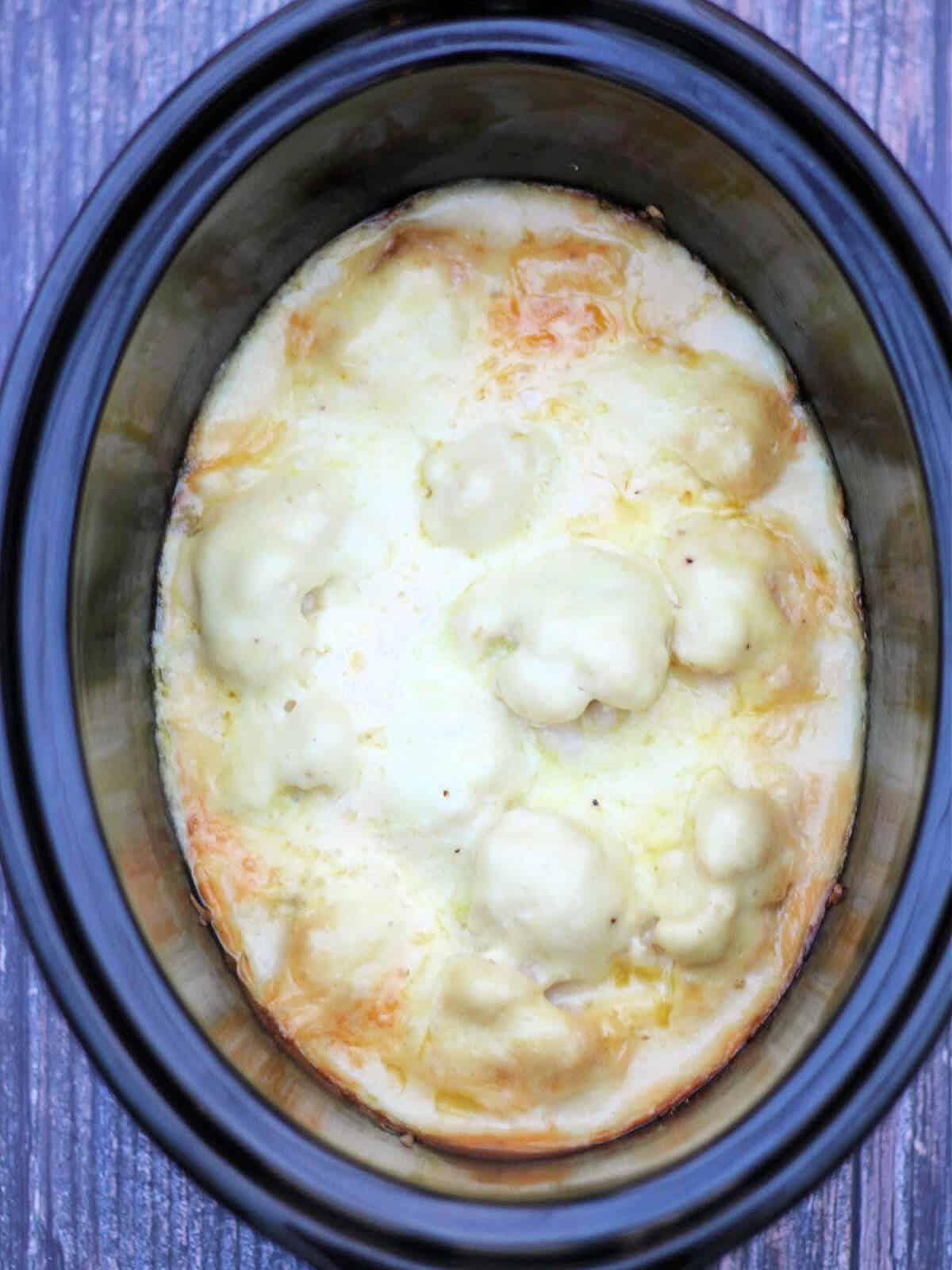 Cooked cauliflower cheese in slow cooker pot.