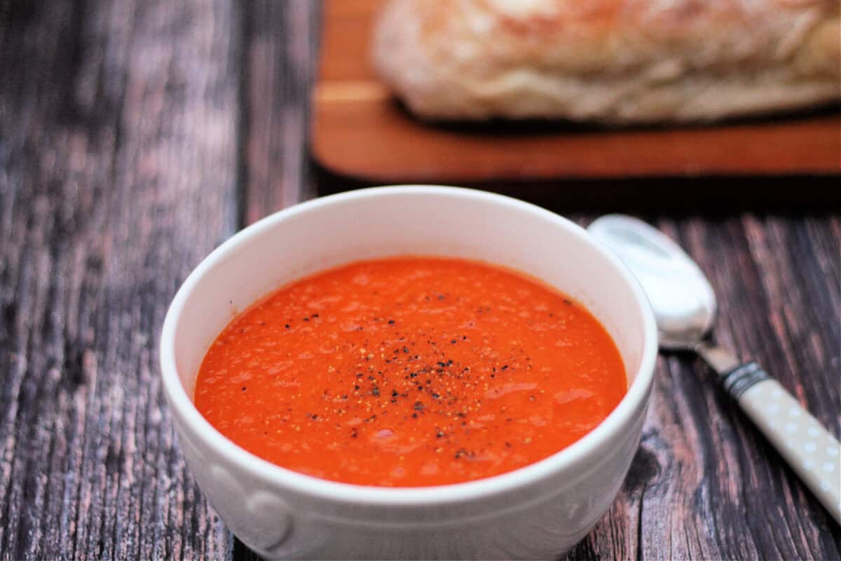 White bowl of tomato soup topped with black pepper.