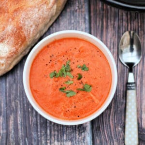 Bowl of tomato soup with basil, bread and spoon to the side.