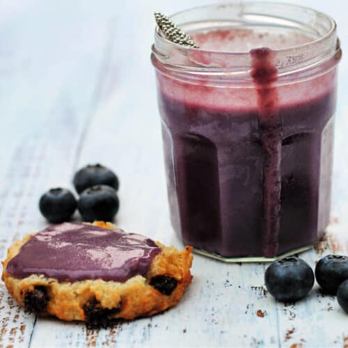 Jar of curd with a drip down the side of it, half a scone spread with blueberry curd beside it.