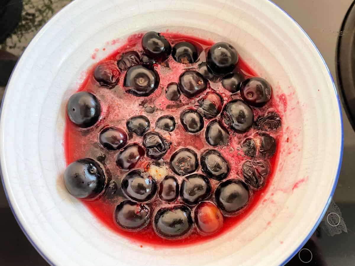 White bowl containing blueberries and pink blueberry juice.