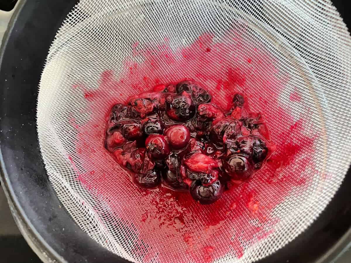 Plastic sieve with cooked blueberries in it, during process of pushing the fruit through the sieve.