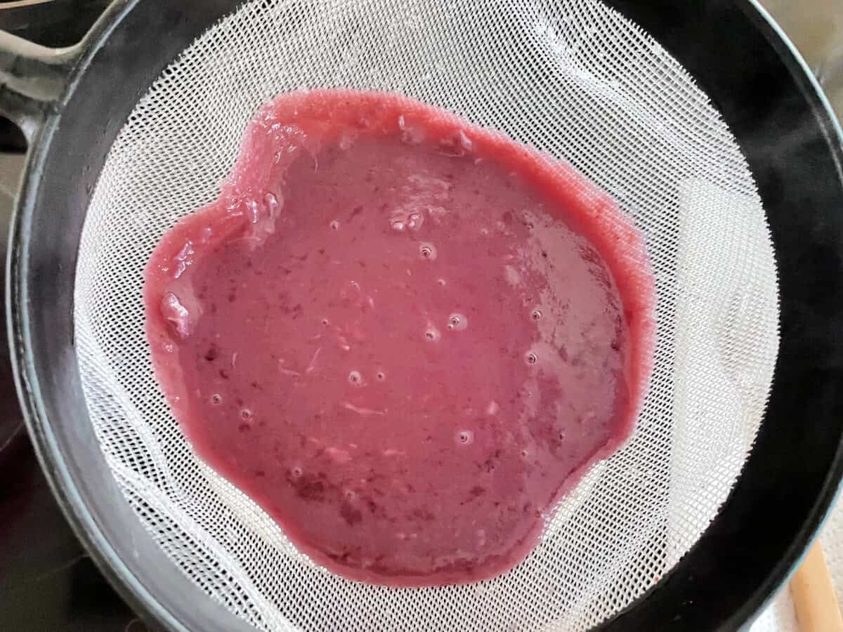 Blueberry curd mixture being strained through a white plastic sieve.