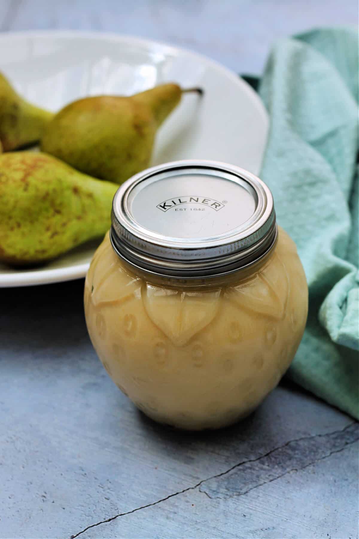 Jar of pear curd in front of a white bowl of pears.