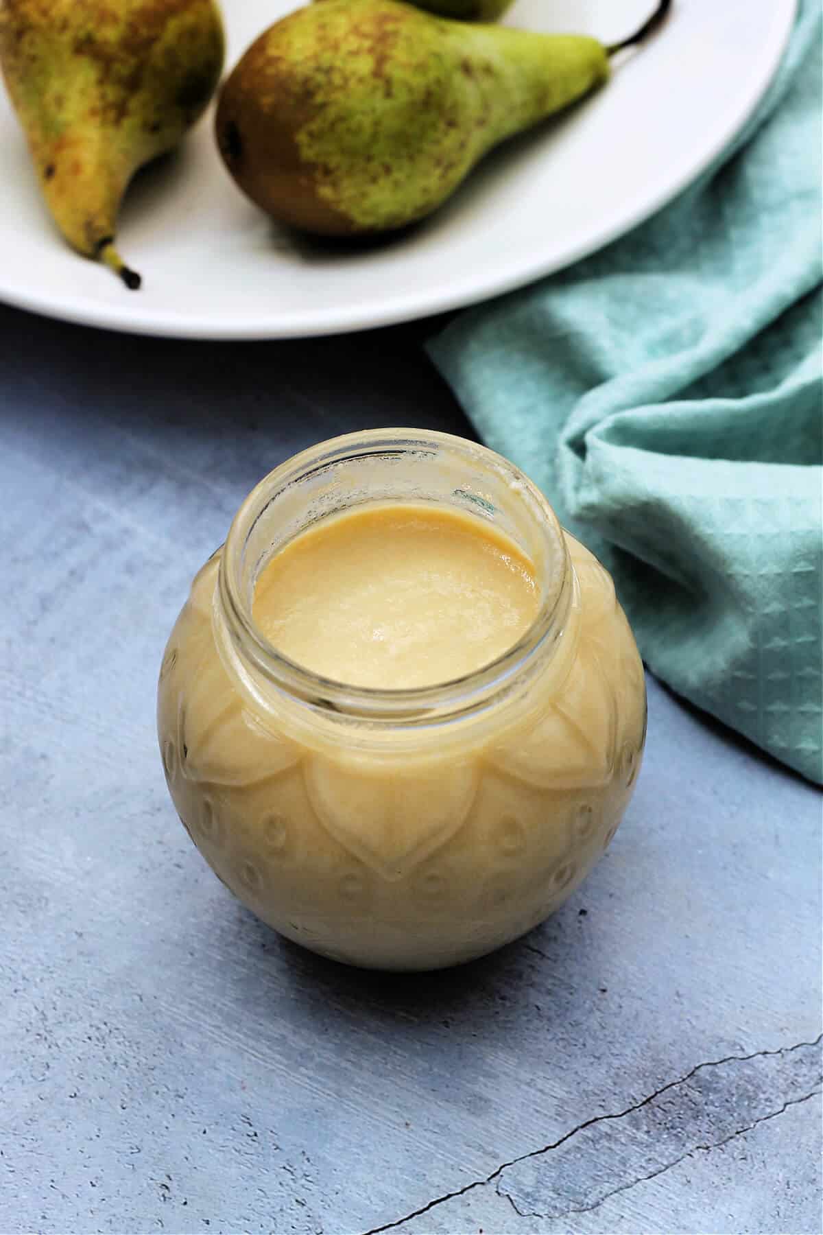 Open jar of yellow coloured pear curd, bowl of pears in background.