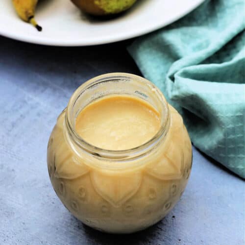Open jar of pear curd with green cloth and pears in background.