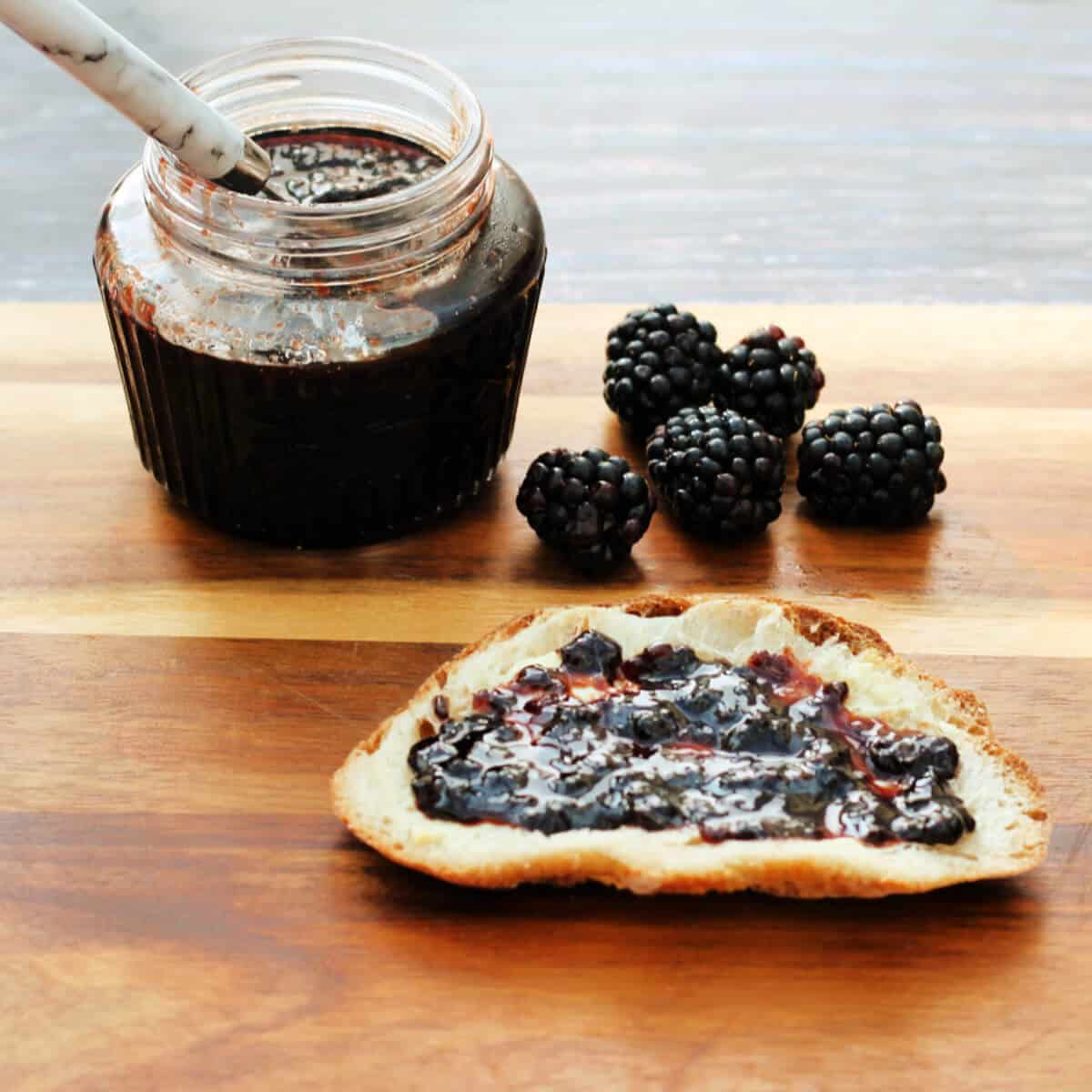 Jam on bread, jam jar and blackberries in background.