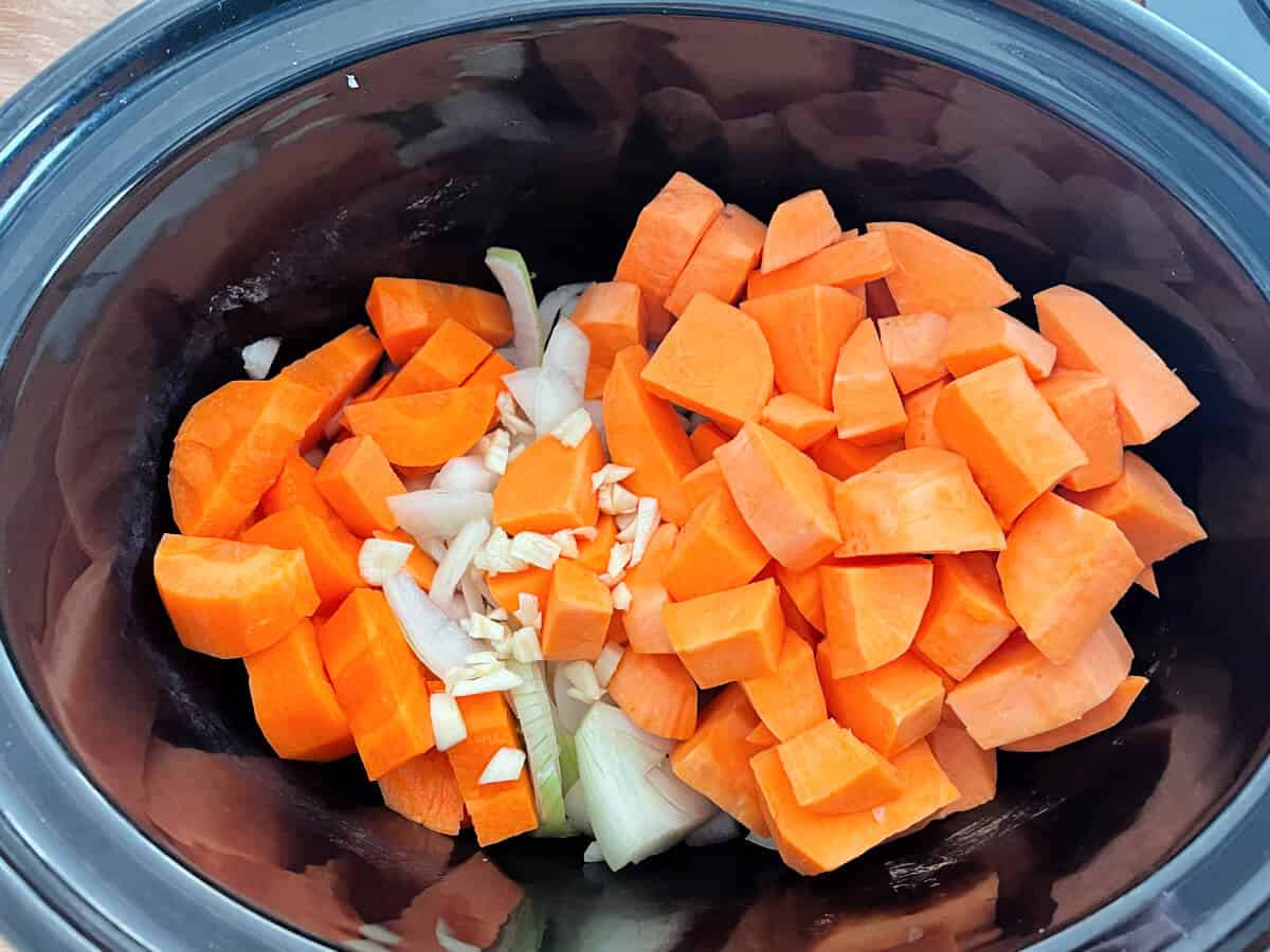 Chopped carrot, onion, garlic and sweet potato in a slow cooker pot.