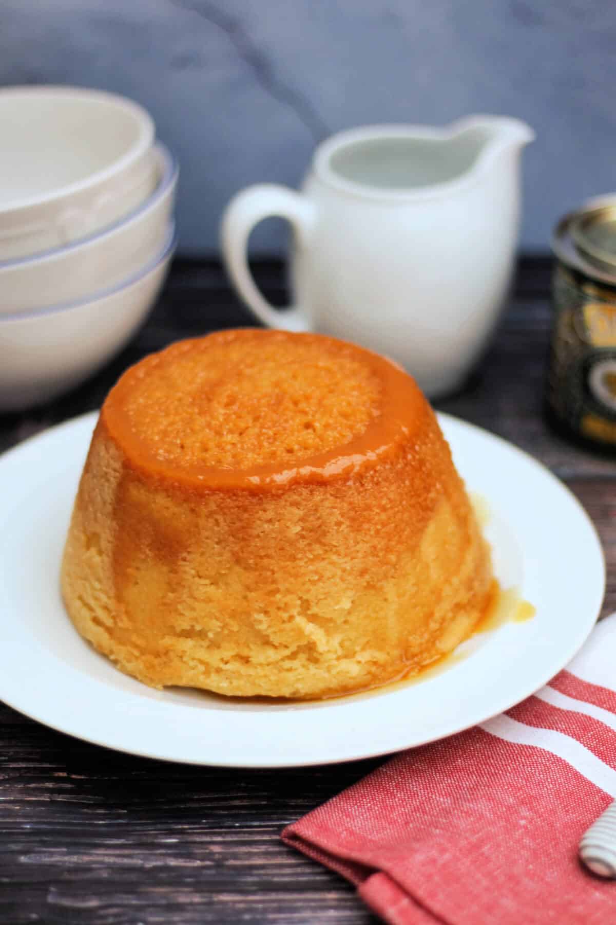 Treacle sponge pudding on a white serving plate, jug of custard and bowls behind.