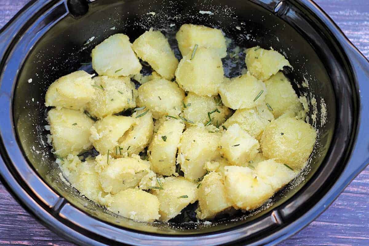Potatoes coated with oil and semolina flour in slow cooker pot.