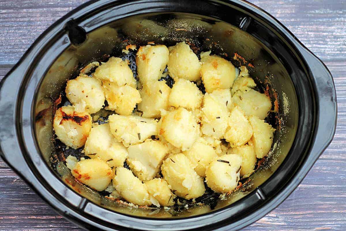 Partly cooked roast potatoes in slow cooker pot.