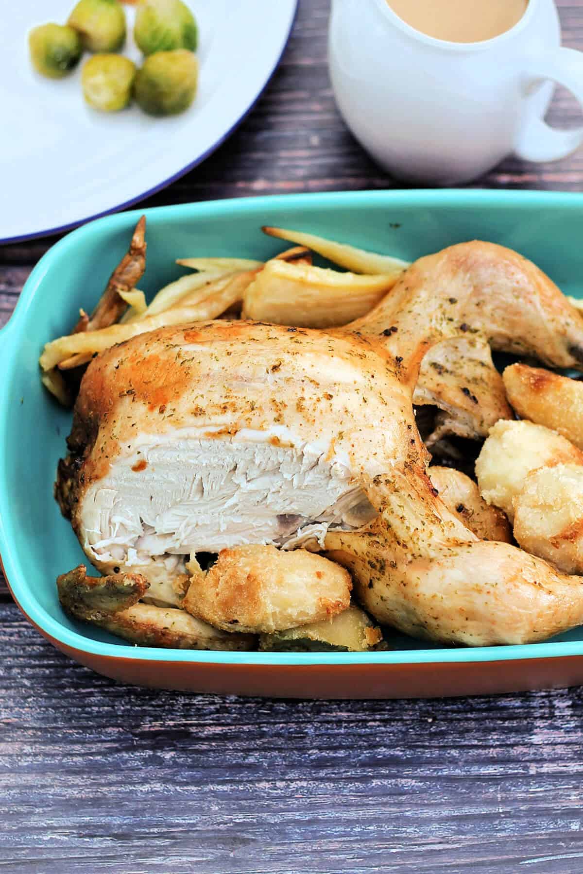 Roast chicken with roast potatoes and parsnips in a serving dish on a table.