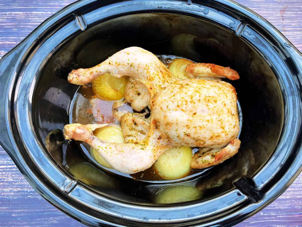 Cooked whole chicken in slow cooker pot.