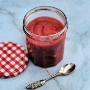 Jar of cranberry curd with lid to left and spoon in front.