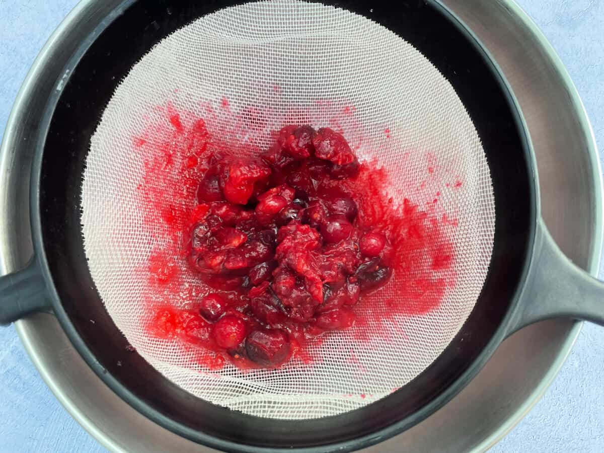 A sieve with cooked cranberries being pressed through it.