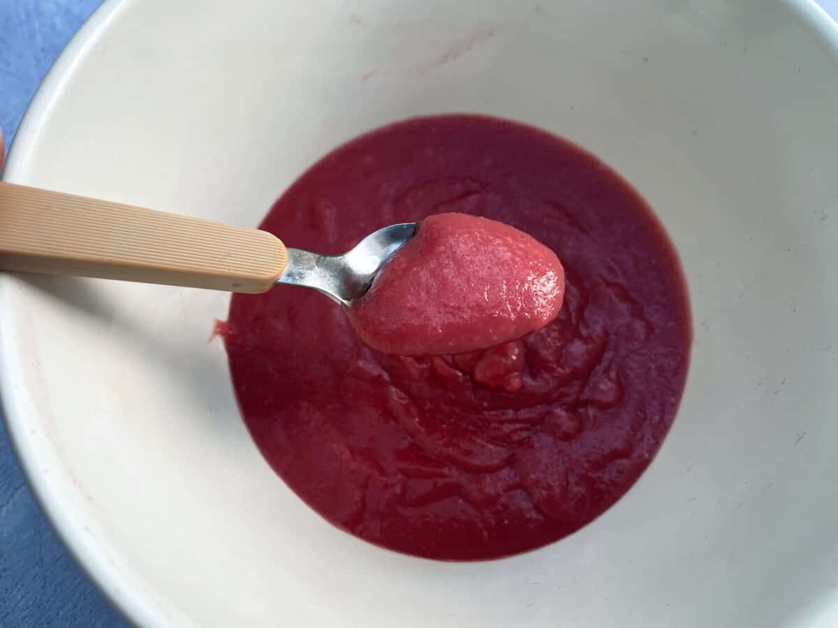 Bowl of finished cranberry curd, teaspoon over it filled with thick curd.
