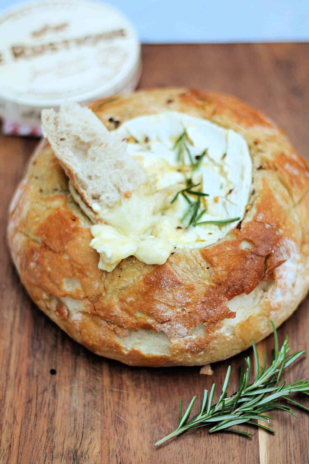 Baked camembert cheese in a bread bowl, with a piece of bread dipped in melting cheese.