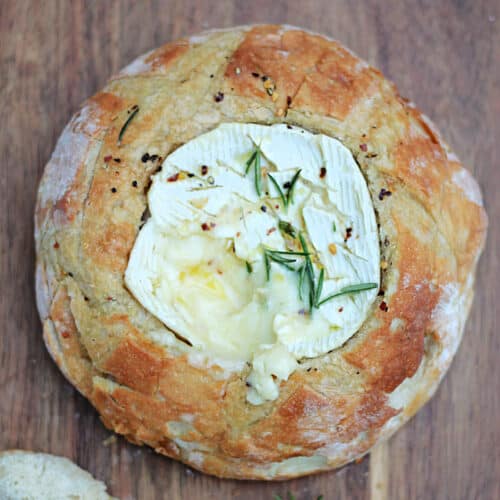 Melting baked camembert cheese in a bread bowl on wooden board.