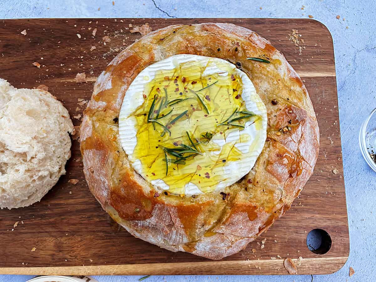 Camembert in bread bowl with oil and herbs drizzled over it.