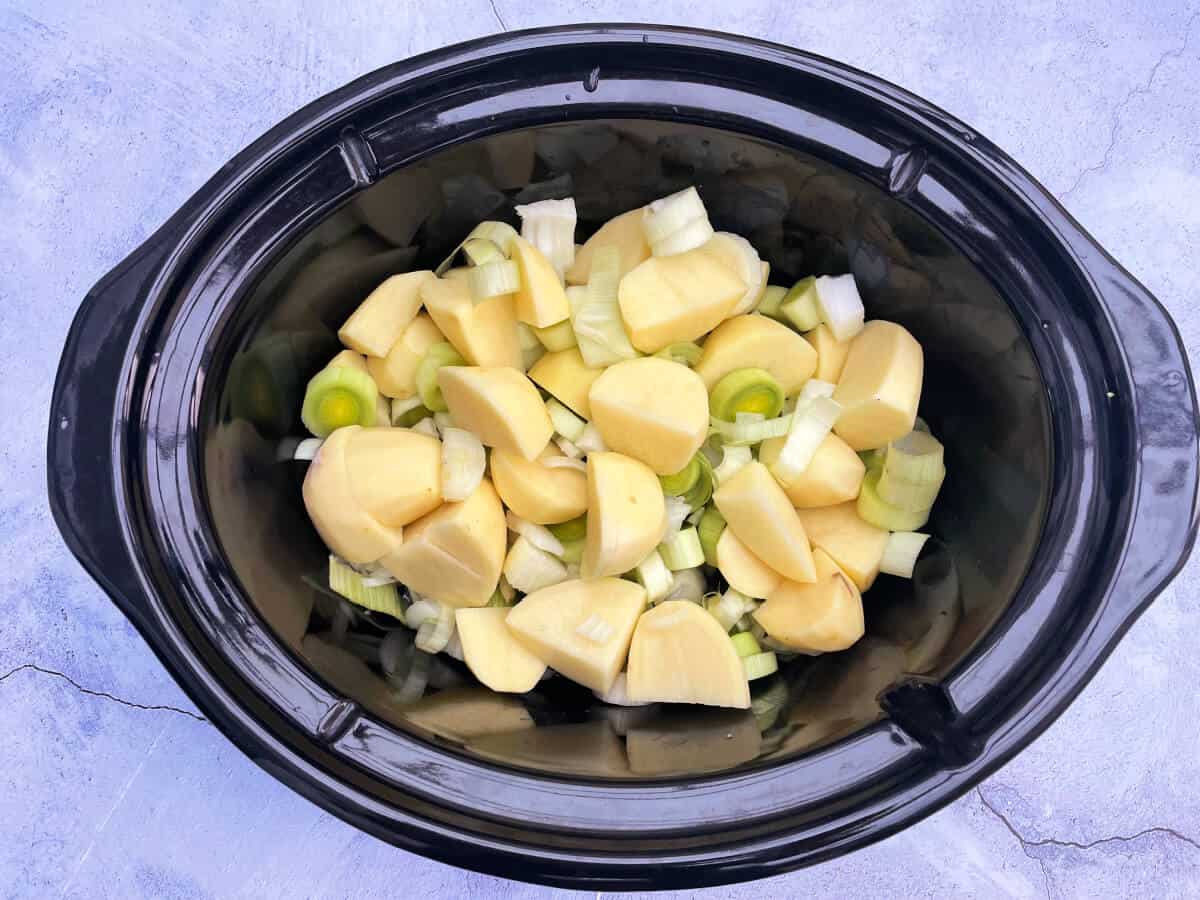 Slow cooker pot with chopped potatoes, leeks, onions and garlic inside.