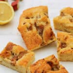 Squares of rhubarb cake on white background, lemon half in background.