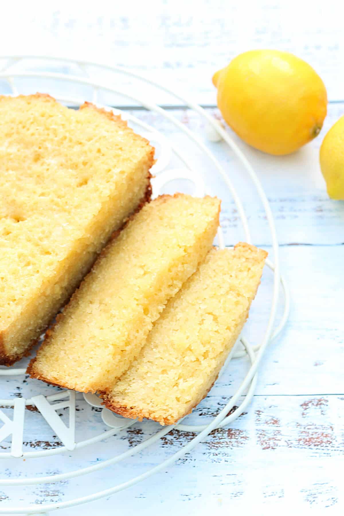 A sliced lemon cake on a cooling rack with lemons in background.