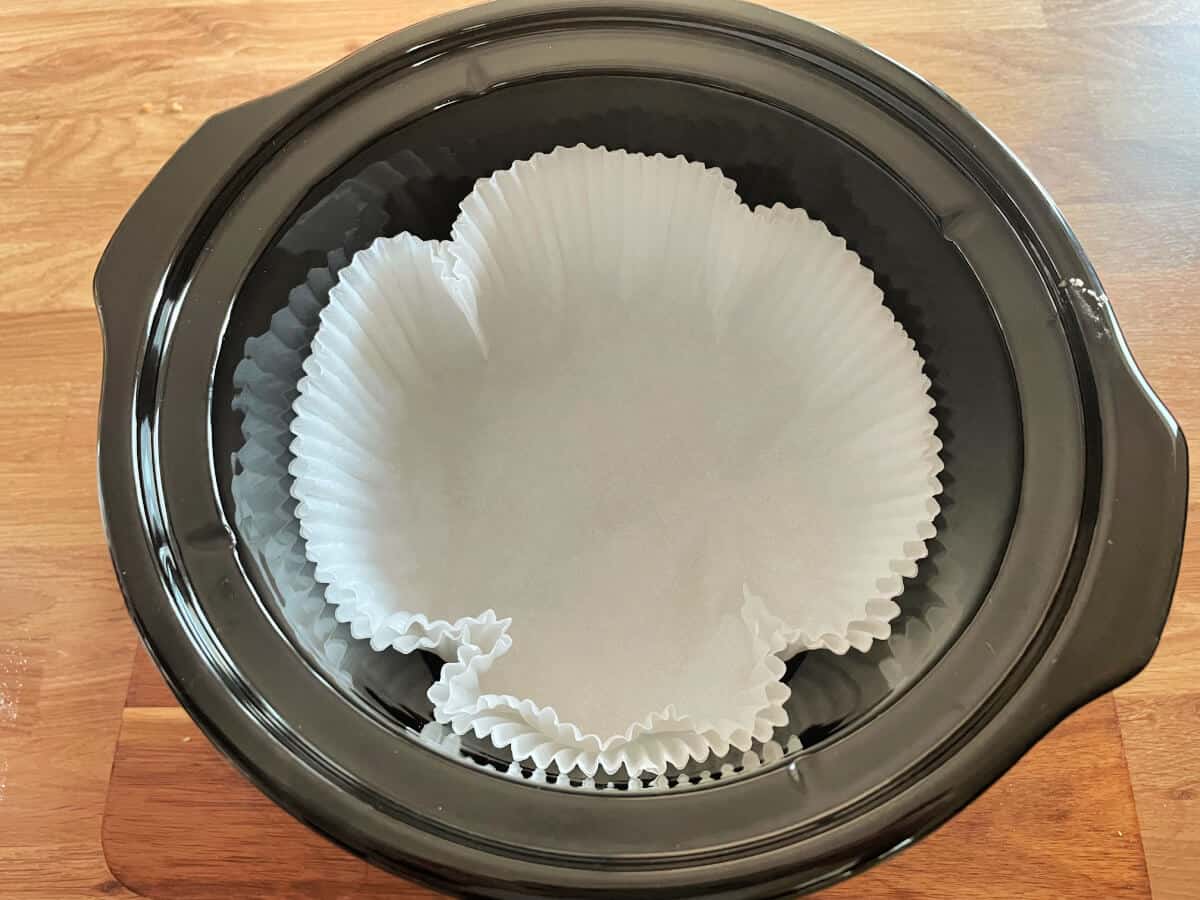 Slow cooker pot with round cake liners inside it.