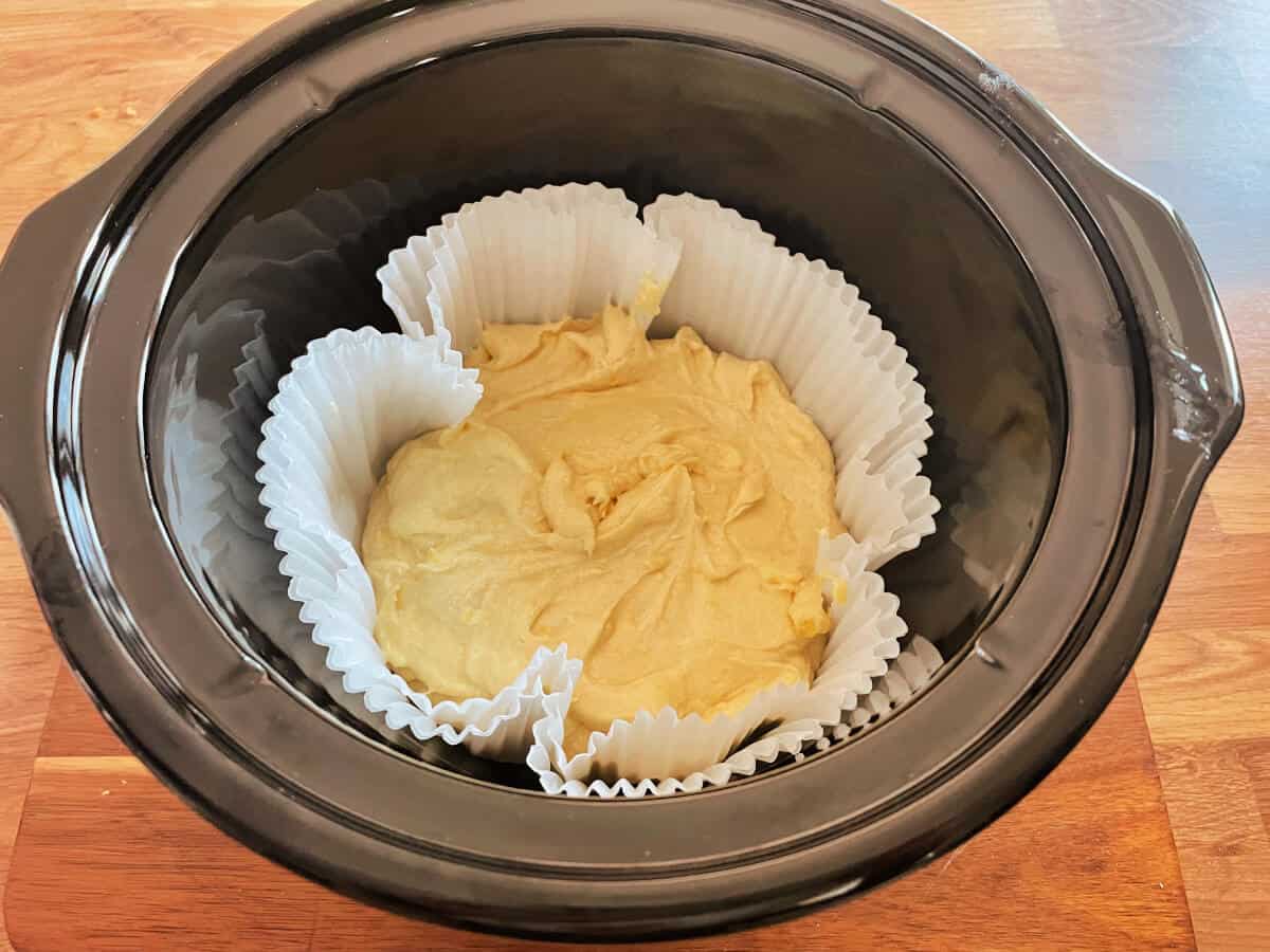 Slow cooker pot with cake mixture inside round cake tin liners, before baking.