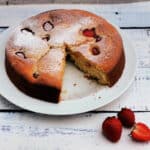 Cake dusted with icing sugar on a white plate, a slice cut out.